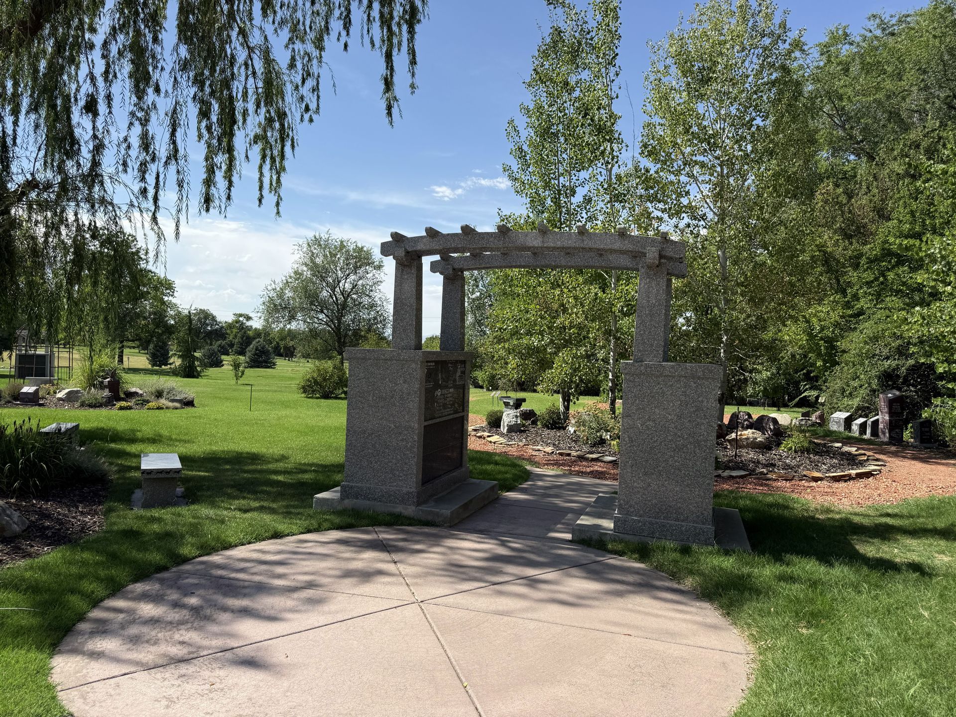 Stone archway in a sunny park with a curved walkway, green lawn, and trees around it