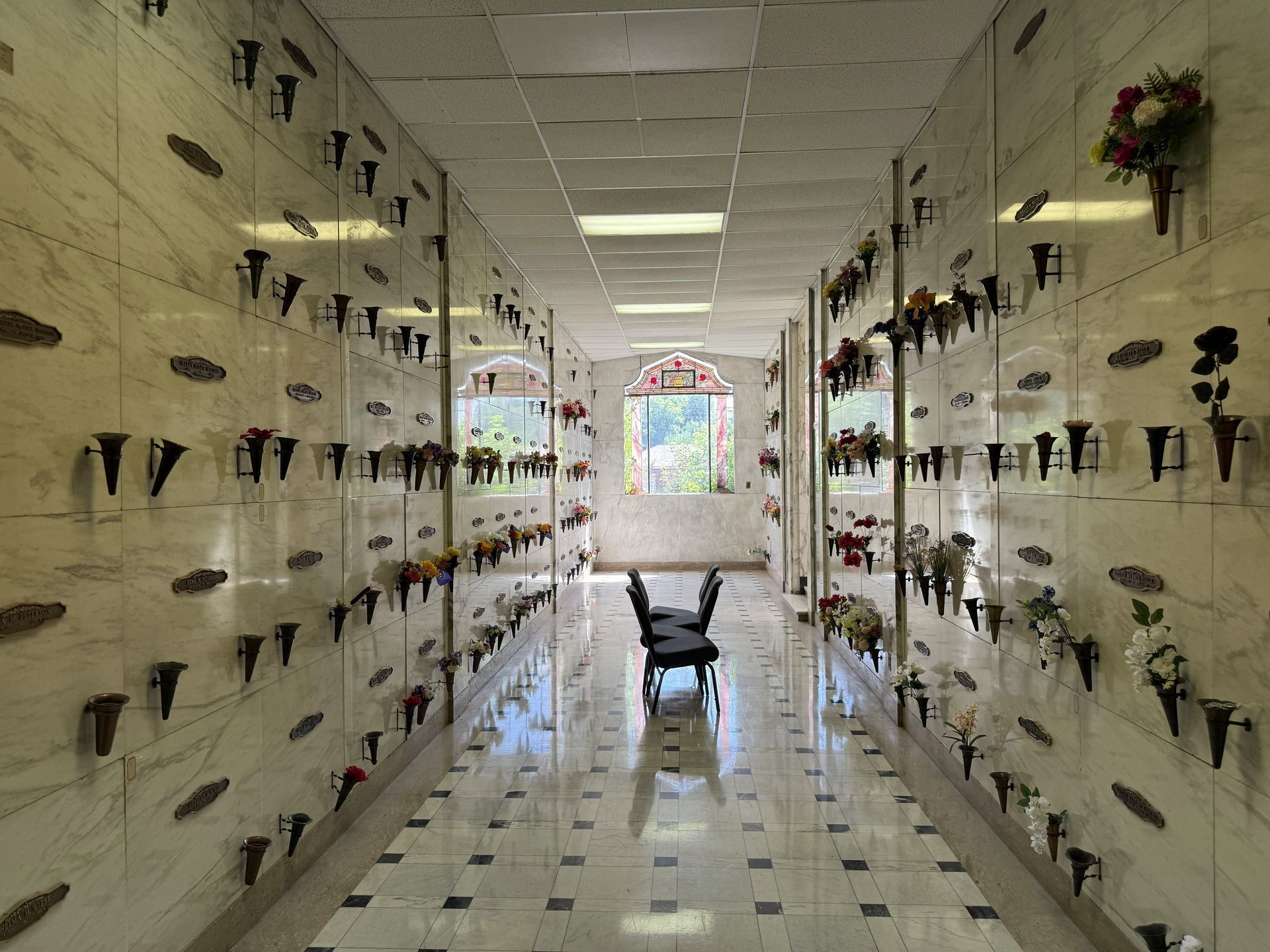 Narrow mausoleum corridor with rows of flower vases on both walls and a chair at the far end.