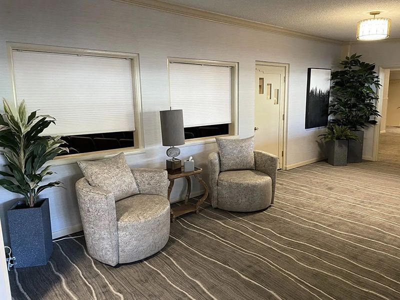 Modern lobby seating area with gray chairs, lamp, windows, and a potted plant