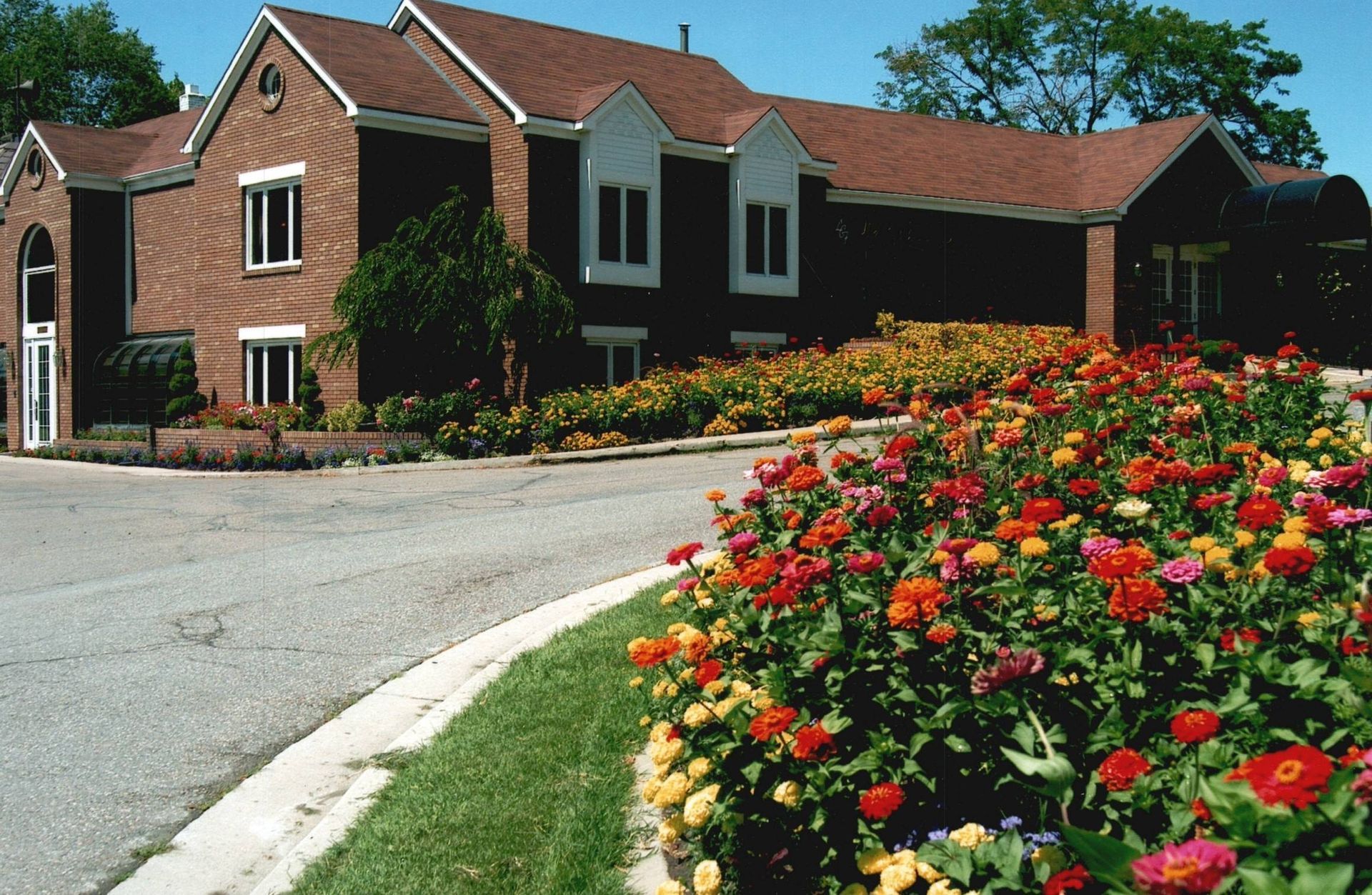 Brick house with red roof beside a curved driveway and a bed of bright flowers