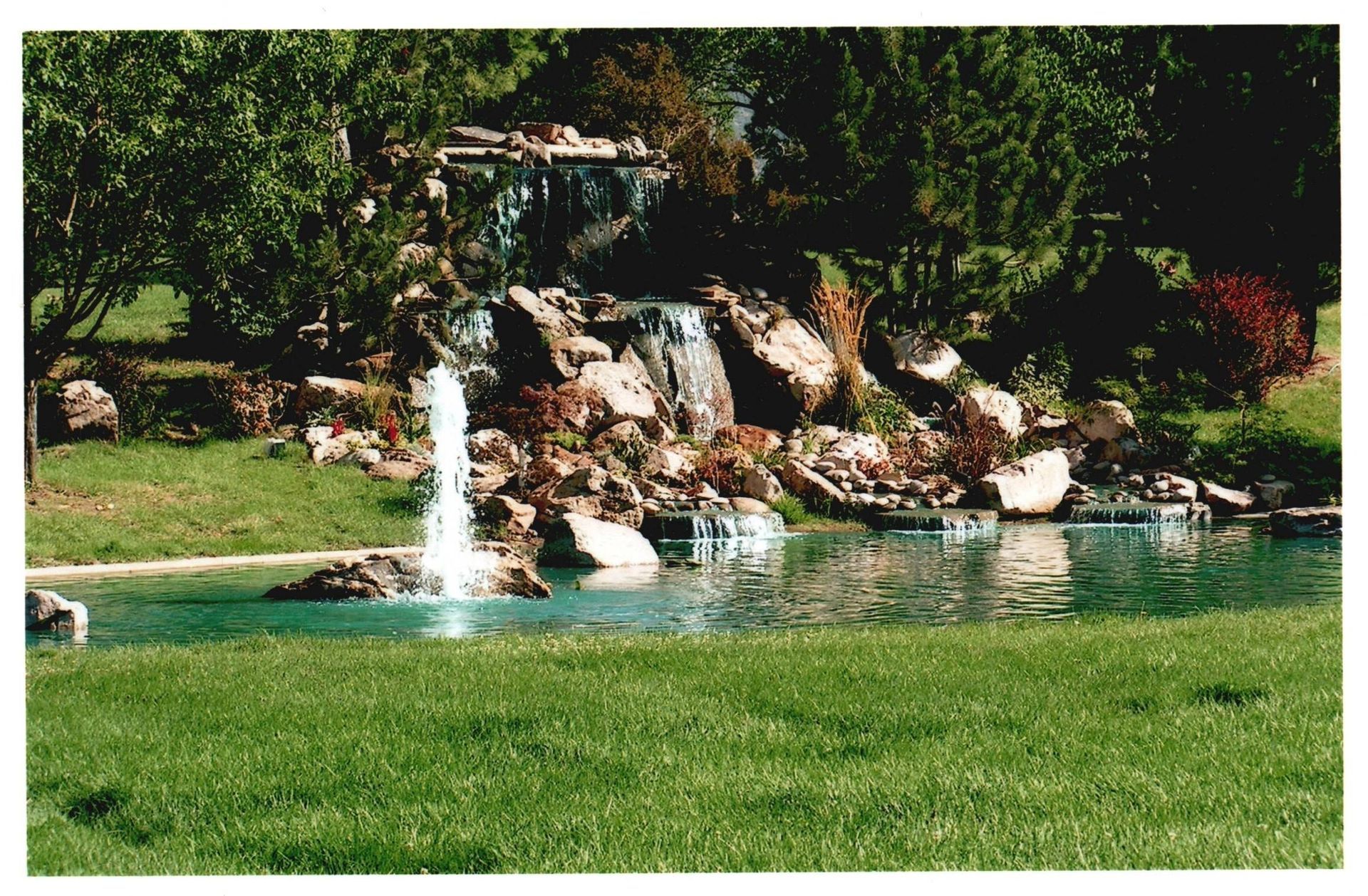 Small waterfall cascading into a pond beside a green lawn and rocky garden