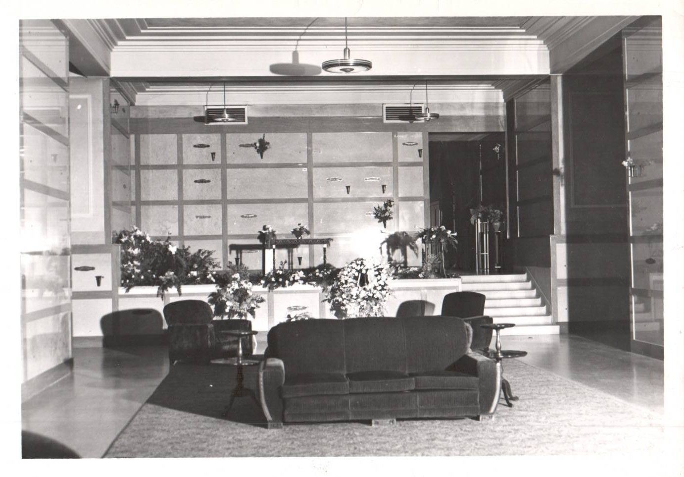 Vintage lobby with sofas, chairs, potted plants, and stairs in a bright, modern interior
