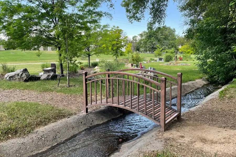Small red footbridge over a creek in a green park with trees and rocks