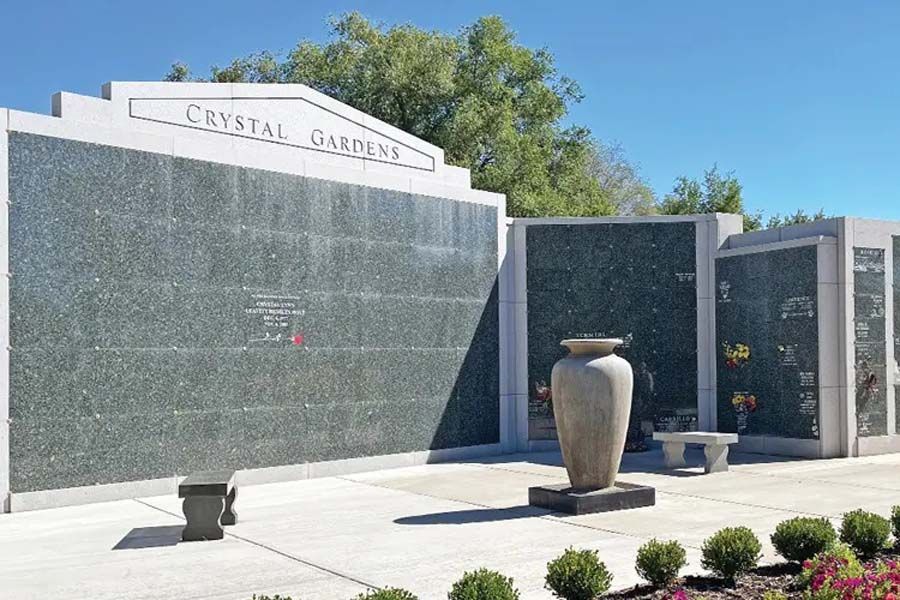 Crystal Gardens memorial wall with large urns and flower beds under a clear blue sky