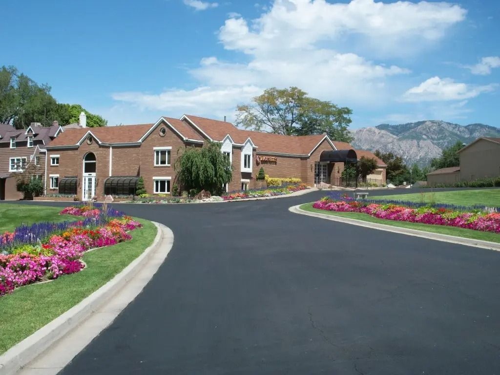 Curved road leading to brick homes with flower beds and mountains under a blue sky