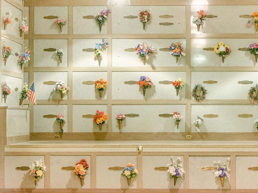 Memorial wall with rows of floral bouquets and brass name plaques under glass.