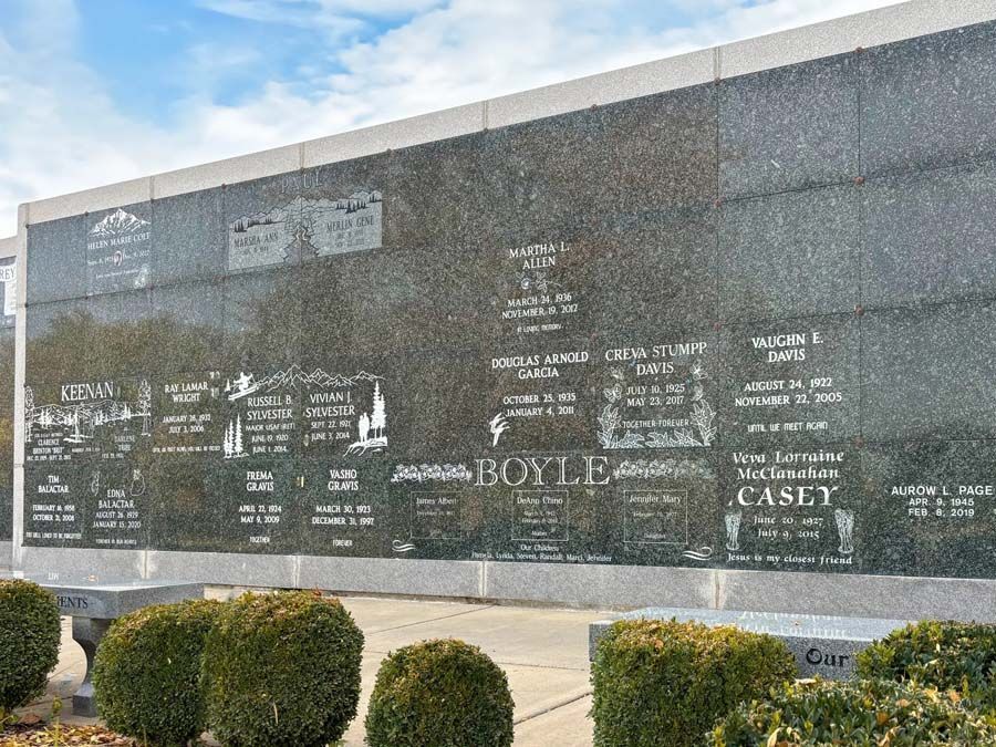 Large polished black memorial wall with engraved names in an outdoor park setting.