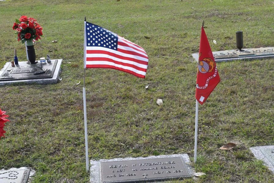 Gravestone with American and Marine Corps flags in a cemetery, with a flower bouquet nearby
