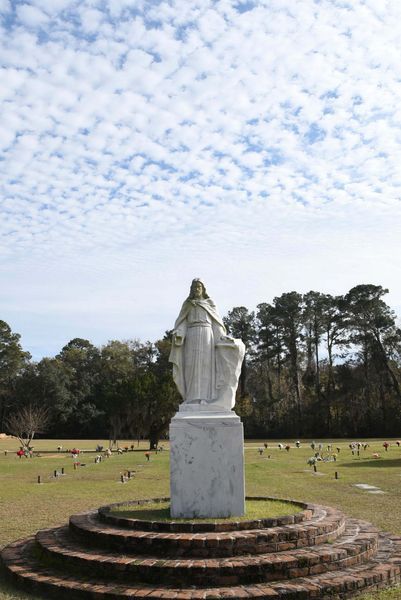 White statue on circular steps in a grassy park under a cloudy sky