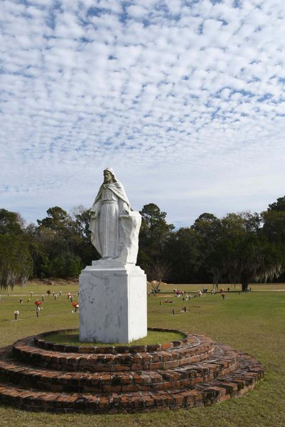 White statue on a brick pedestal in a grassy park under a cloudy sky