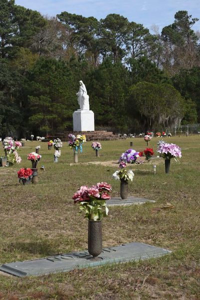 Memorial cemetery with white statue and rows of colorful flower arrangements on grave markers