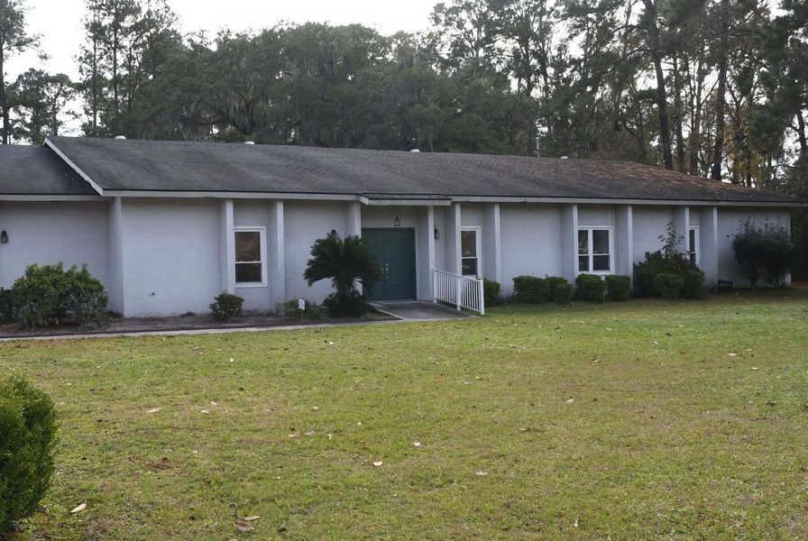 Single-story white house with a dark roof and front lawn, seen from the street.