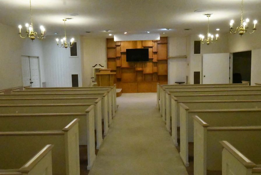 Empty church sanctuary with rows of pews facing a wooden altar and pulpit.