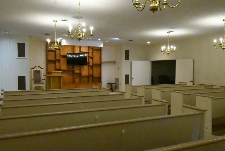 Empty church sanctuary with wooden pews, chandeliers, and a stage at the front