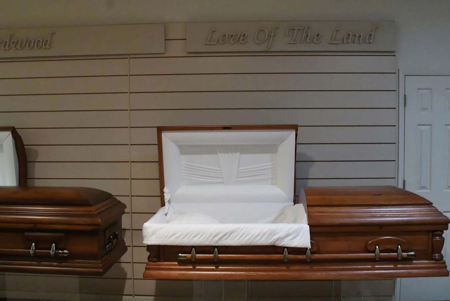 Open white casket centered between two brown caskets in a funeral showroom