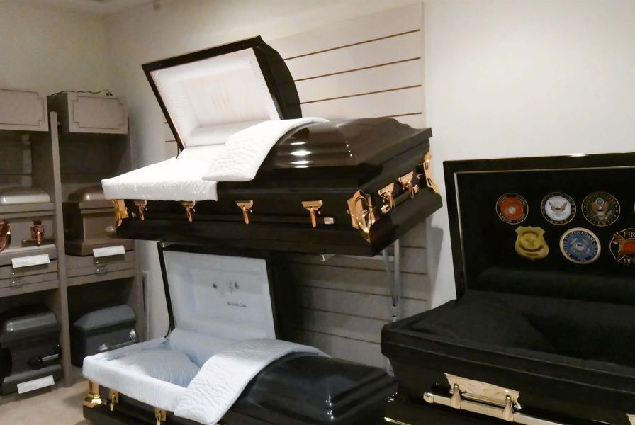 Open caskets displayed on shelves in a showroom, including a black casket with patches on the right.