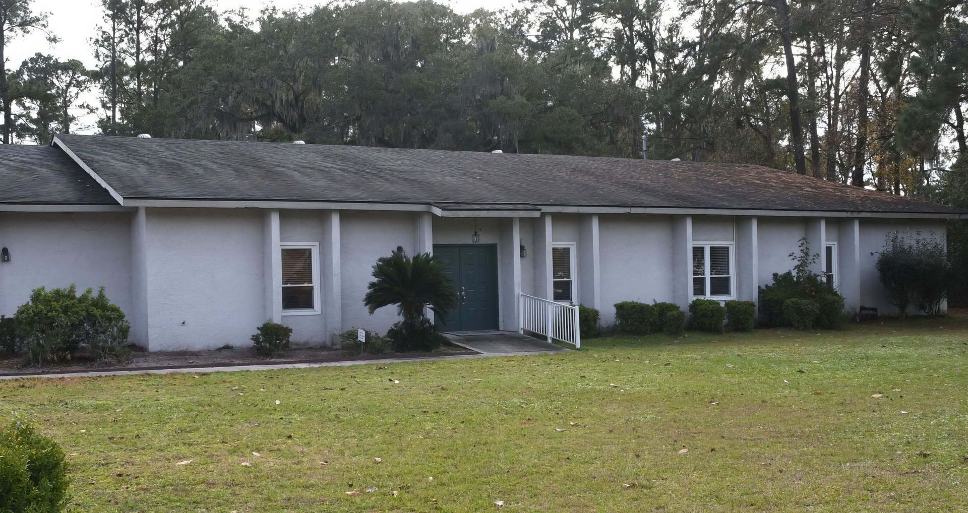 Single-story white house with a front porch and large grassy yard, trees in the background