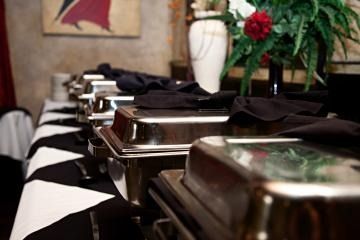 Covered buffet chafing dishes lined up on a black-and-white tablecloth at a catered event