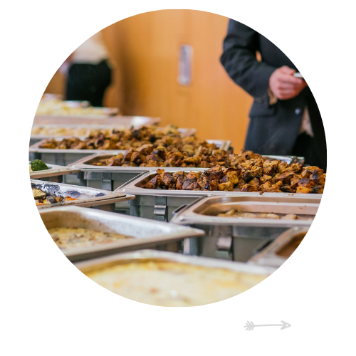 Buffet trays of roasted food with a person in a dark coat serving in the background