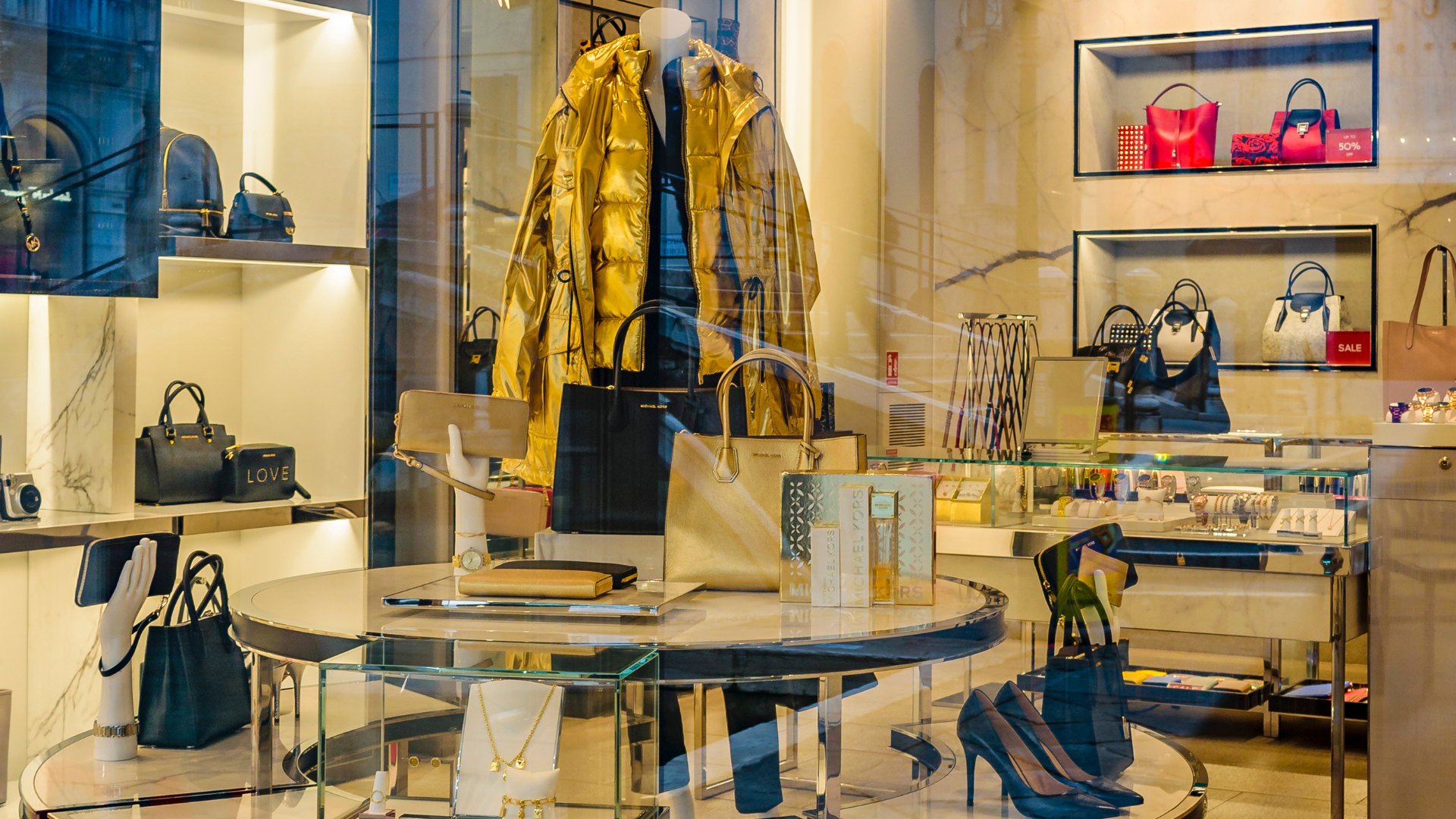 Luxury boutique interior with designer handbags, shelves of accessories, and a yellow coat on display