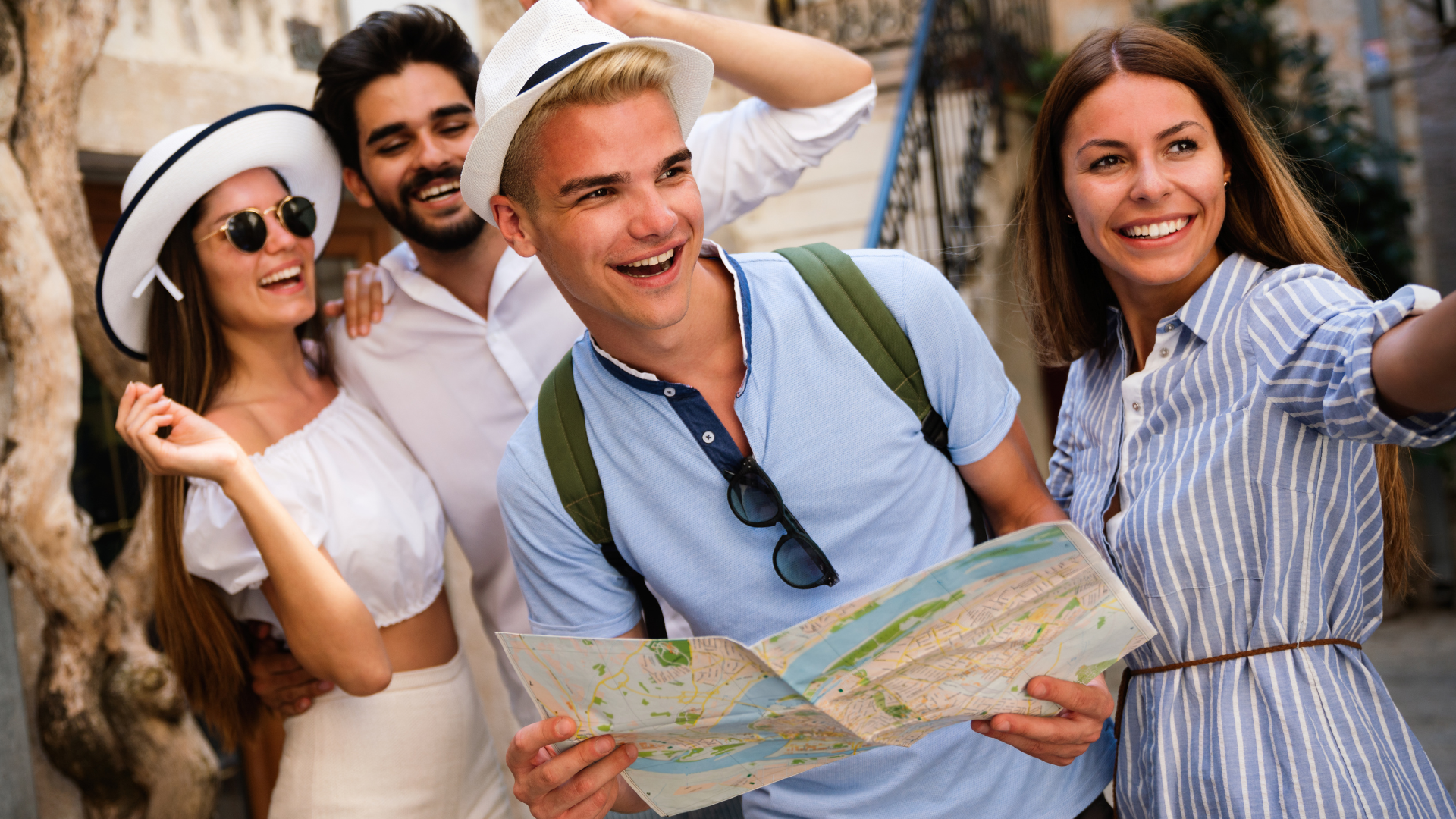 Friends smiling and holding a map outdoors, posing for a travel photo in a sunny setting
