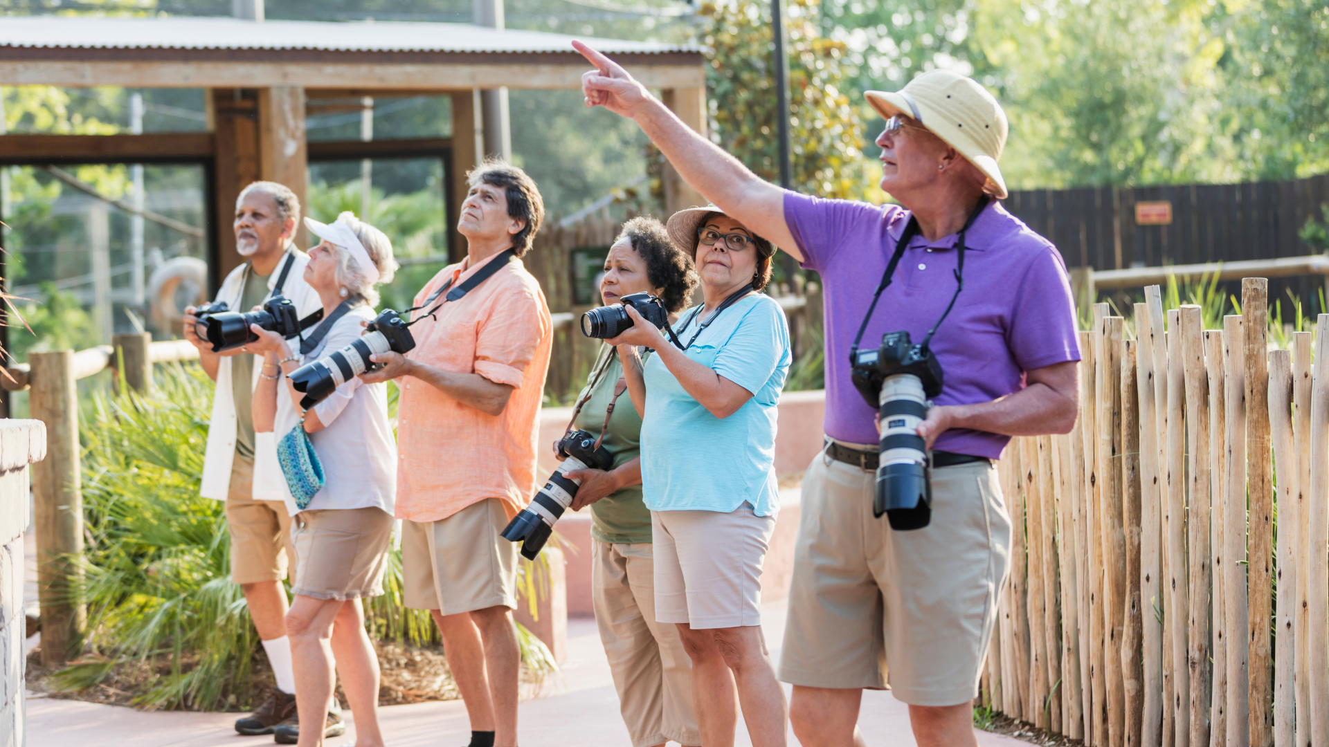 Group of photographers with cameras outdoors, one pointing ahead while others look on.