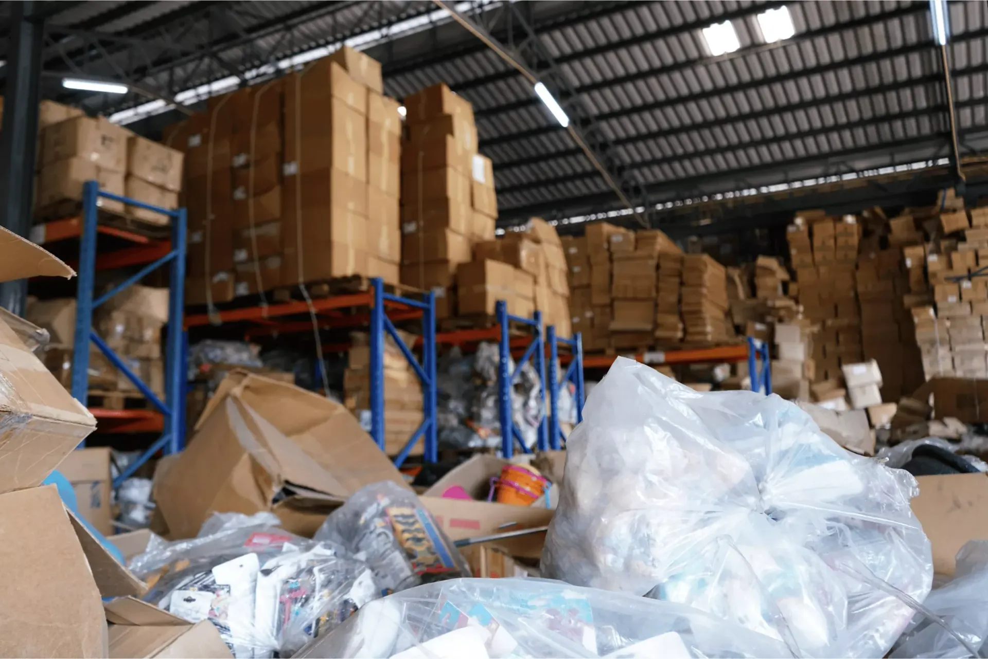 A cluttered warehouse featuring tall metal shelving units stacked with cardboard boxes and debris scattered on the floor.