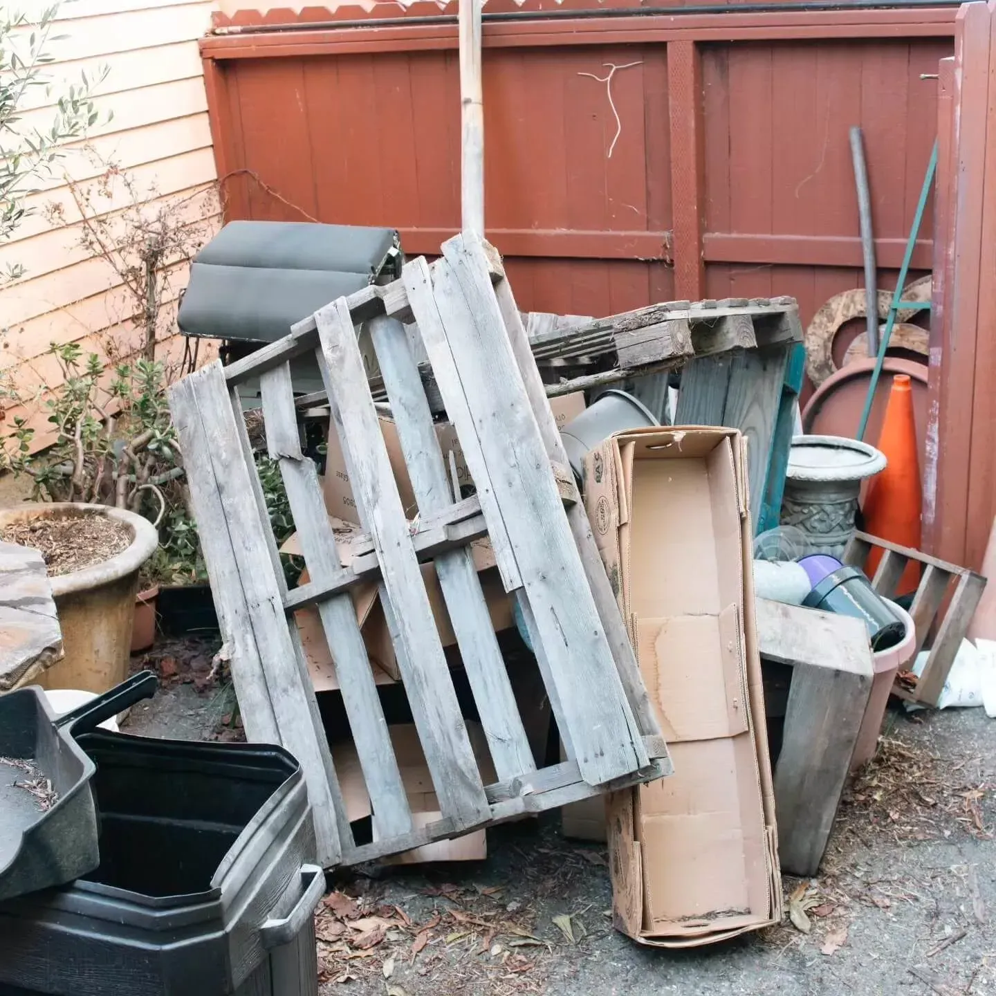 A pile of discarded wooden pallets, a cardboard box, and various garden items against a wooden fence in Ventura, CA