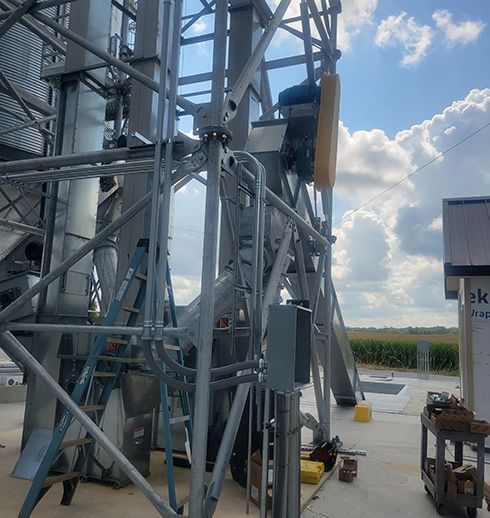 Grain elevator under construction with gray metal framework, wiring, and a ladder.