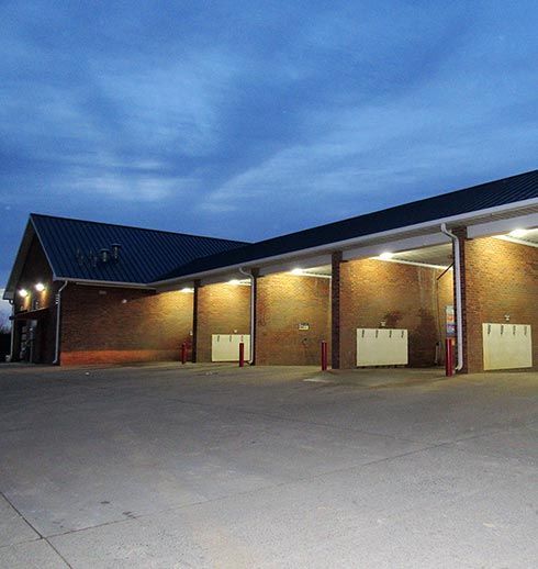 Car wash exterior at dusk; brick building, open bays, blue sky.