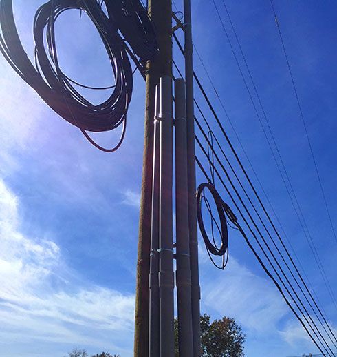 Utility pole with bundled wires and cables against a blue, cloudy sky.