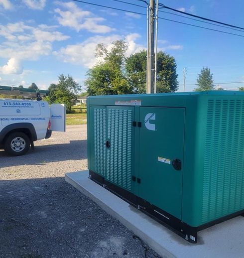 Green Cummins generator on concrete pad, with service truck in background. Outdoors, cloudy sky.