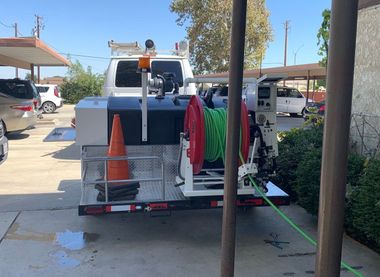 White utility truck with traffic cone and hoses parked in a driveway, with houses in the background