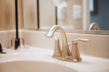 Close-up of a chrome bathroom faucet and sink with a mirror reflection in the background