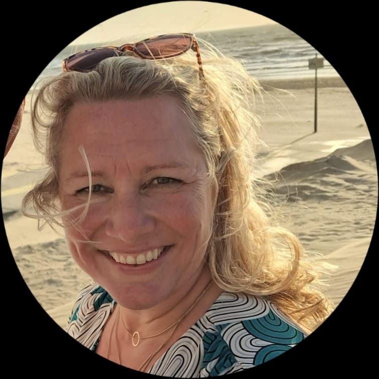 Een vrouw lacht op het strand, met een zonnebril op haar hoofd. De lucht en het zand zijn achter haar zichtbaar.