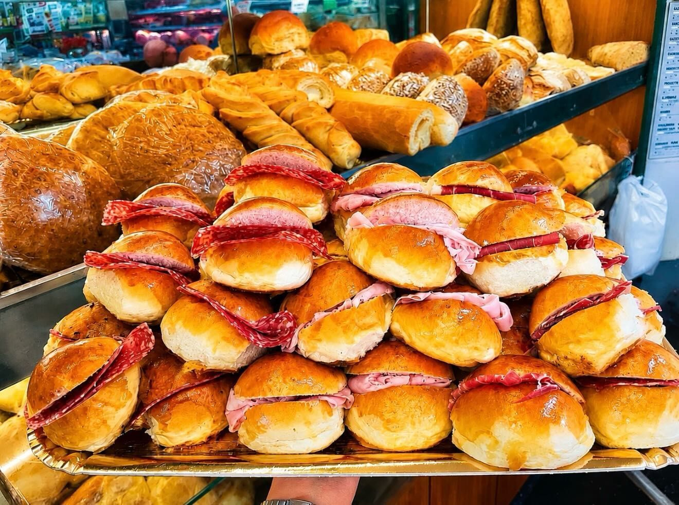 Vassoi di panini e pasticcini assortiti in esposizione in una panetteria.