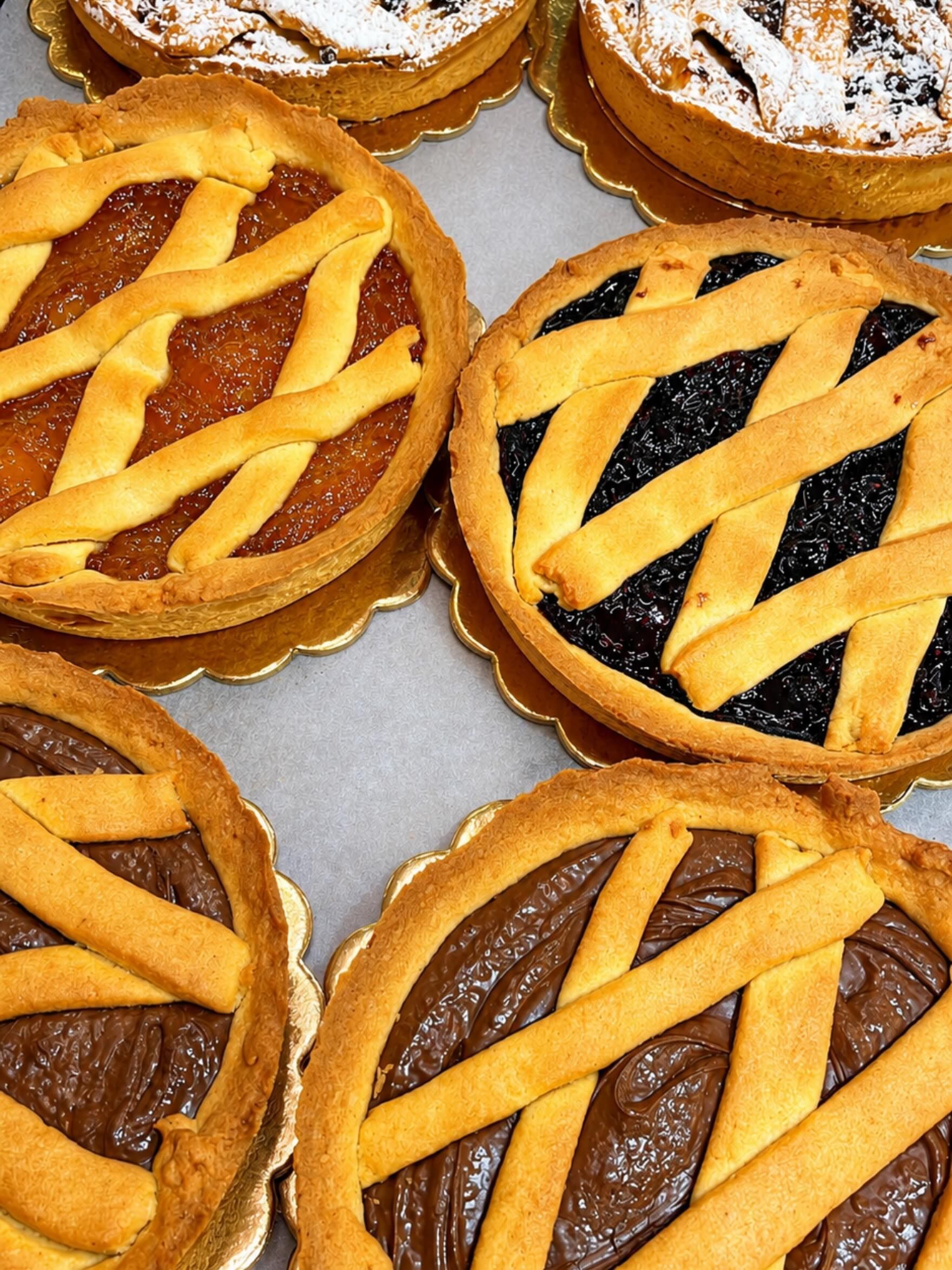 Assortimento di mini crostatine di frutta con copertura a griglia, alcune spolverate di zucchero a velo, disposte su un vassoio.