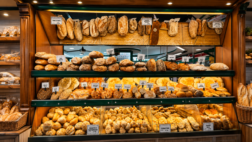Vetrina di una panetteria con scaffali pieni di pasticcini, pane e prodotti da forno assortiti, in un accogliente negozio in legno.