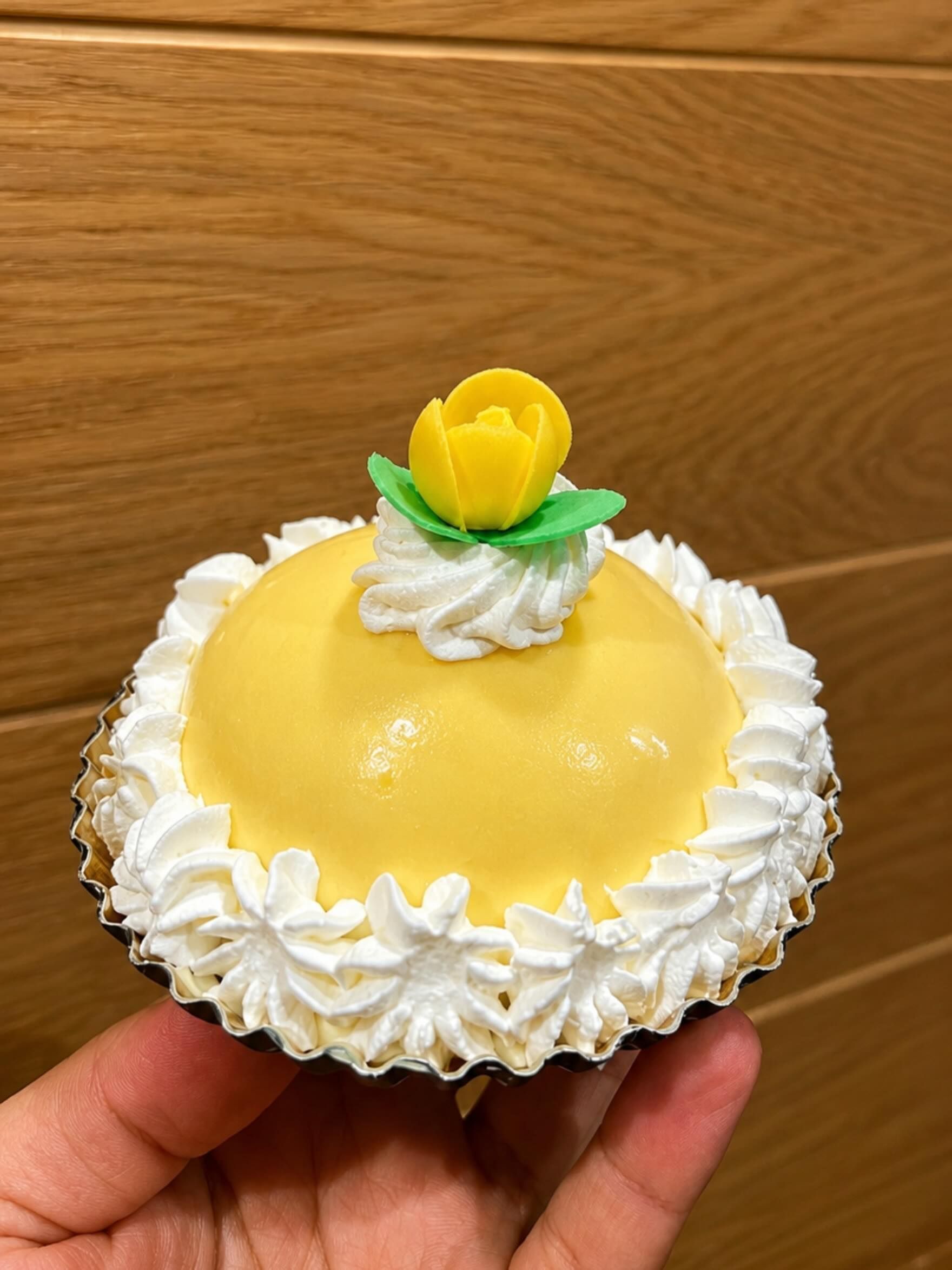 Cupcake con glassa gialla, decorato con crema bianca fatta con sac à poche e un piccolo fiorellino giallo in cima, tenuto in mano.