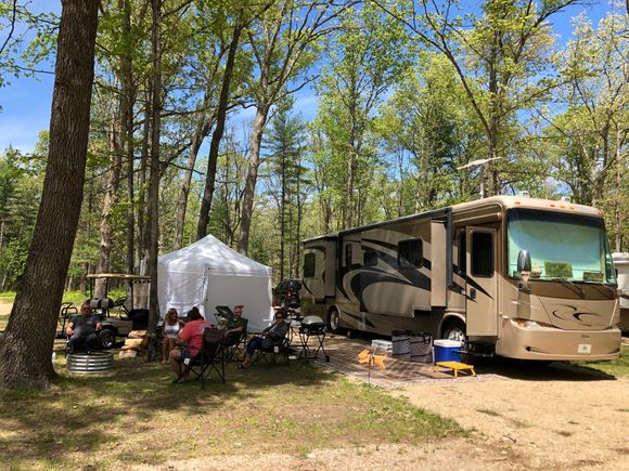 A rv is parked in a campground surrounded by trees.