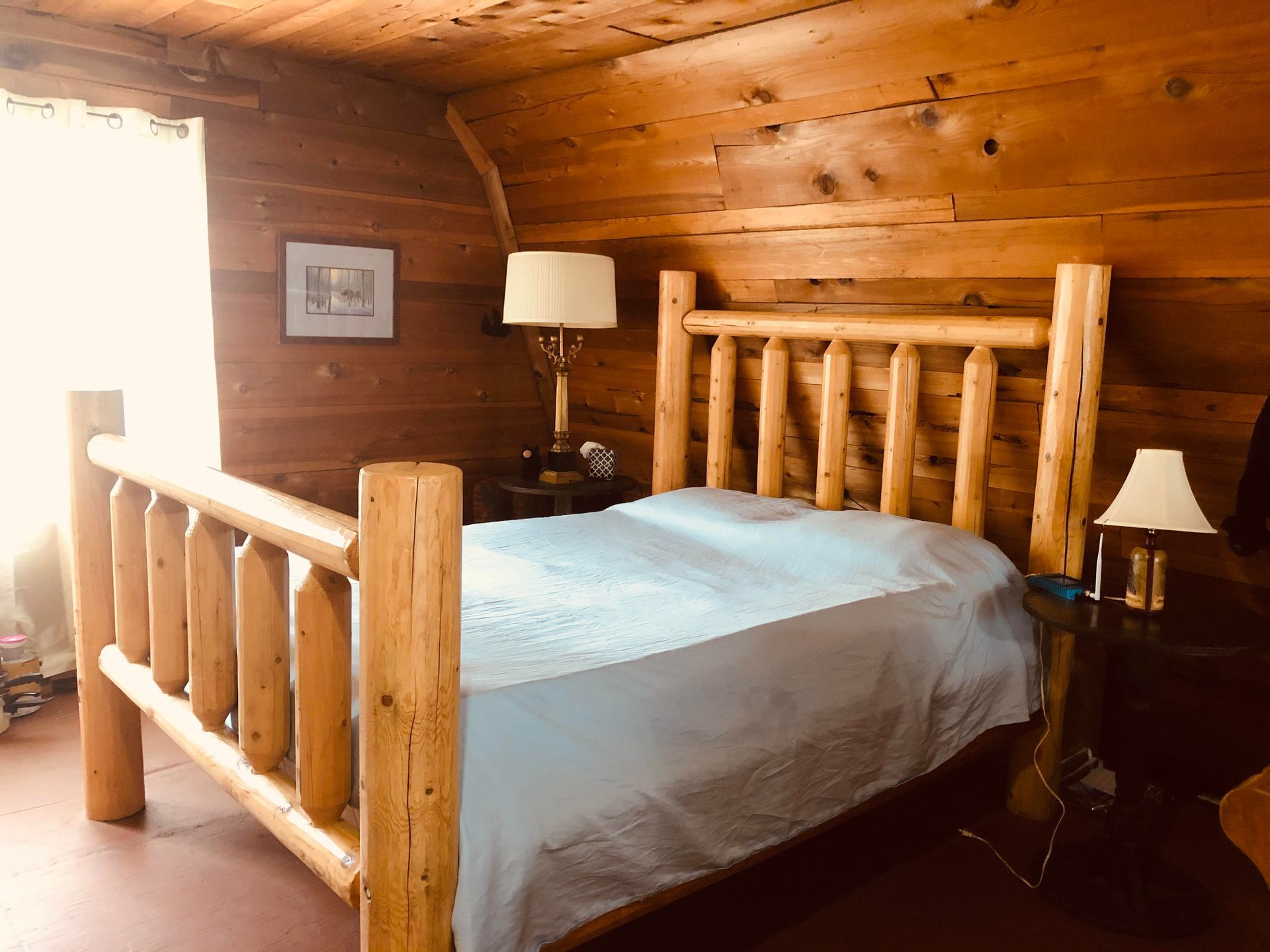 A bedroom in a log cabin with a log bed and two lamps.