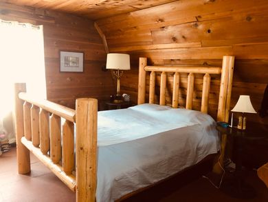 A bedroom in a log cabin with a log bed and two lamps.