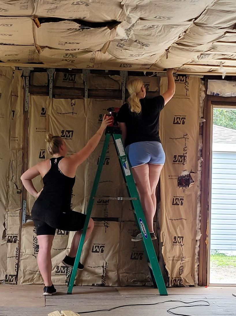 Two women are working on the ceiling of a building.