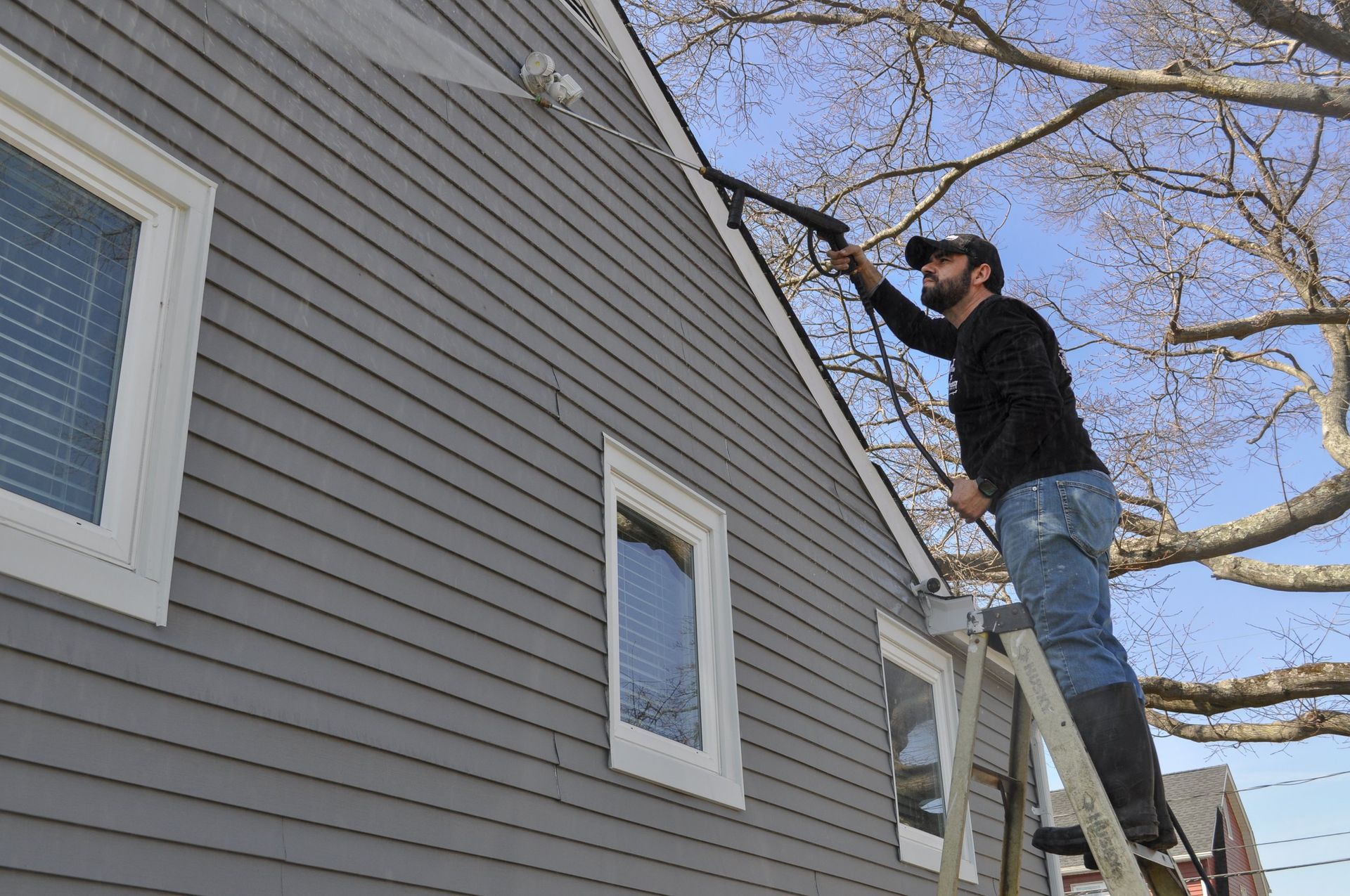 Person on a ladder painting the side of a gray house