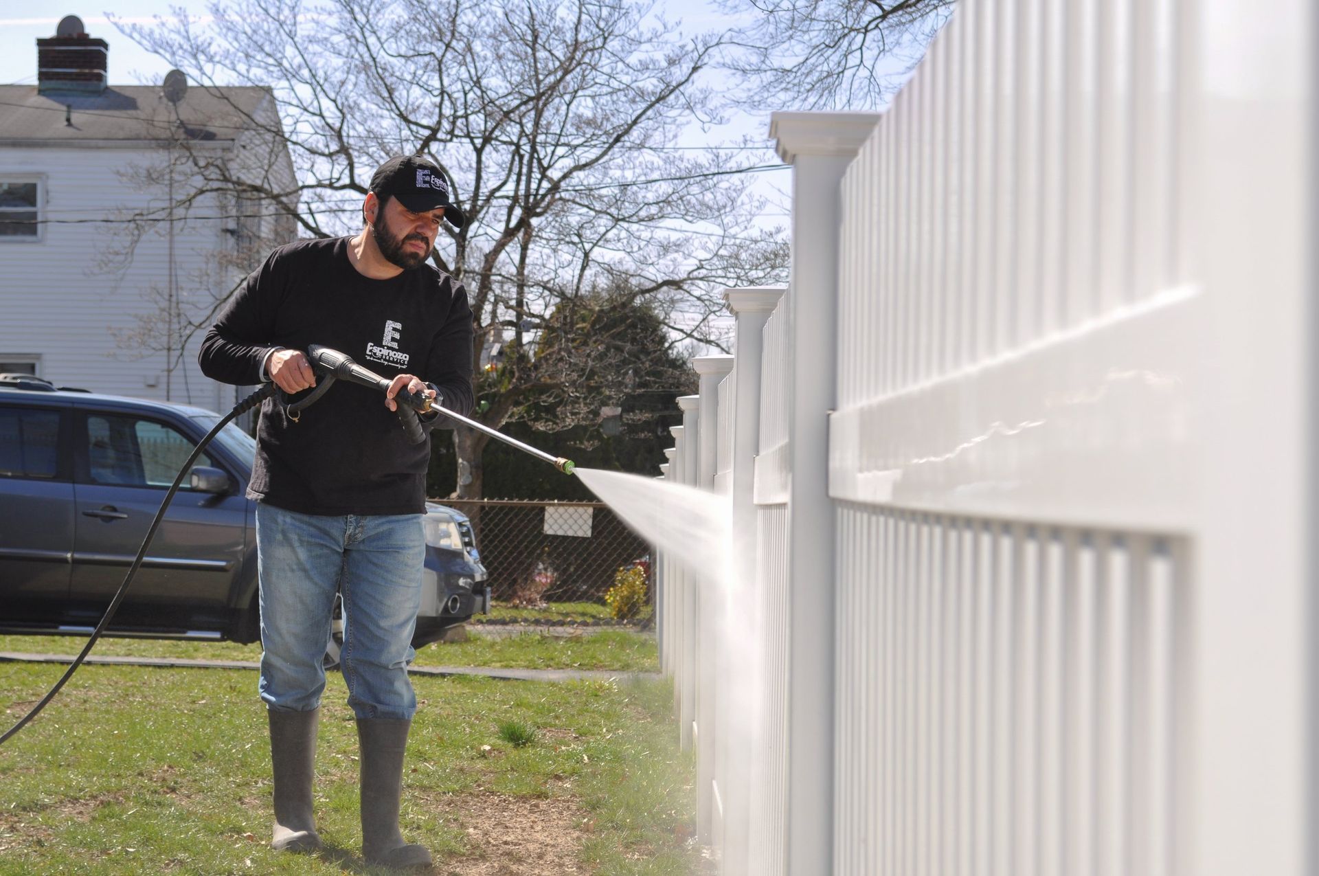 Man pressure-washes a white fence in a yard on a sunny day.