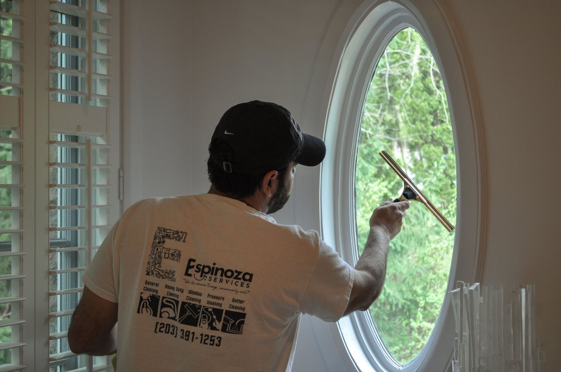 Worker cleaning a large oval window with a squeegee in a bright room