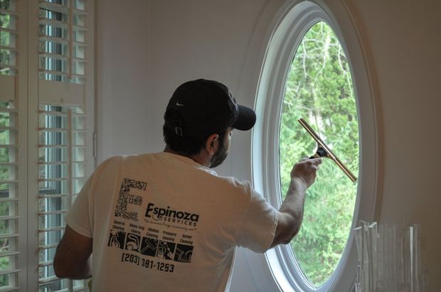 Worker cleaning a large oval window with a squeegee in a bright room