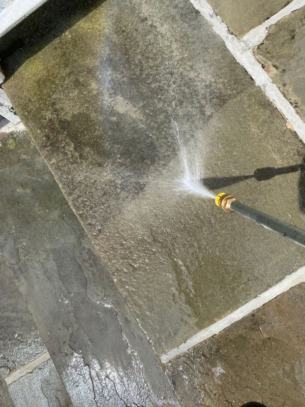 Water spraying onto a wet stone patio from a hose nozzle