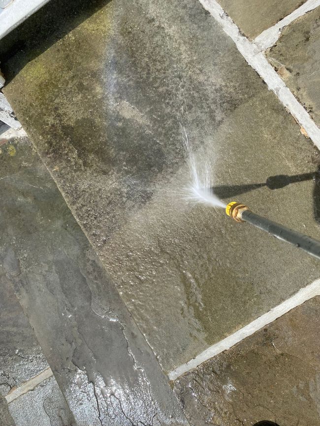 Water spraying onto a wet stone patio from a hose nozzle