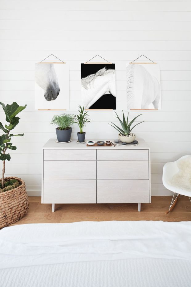 Bright minimalist bedroom with white dresser, wall art, and potted plants